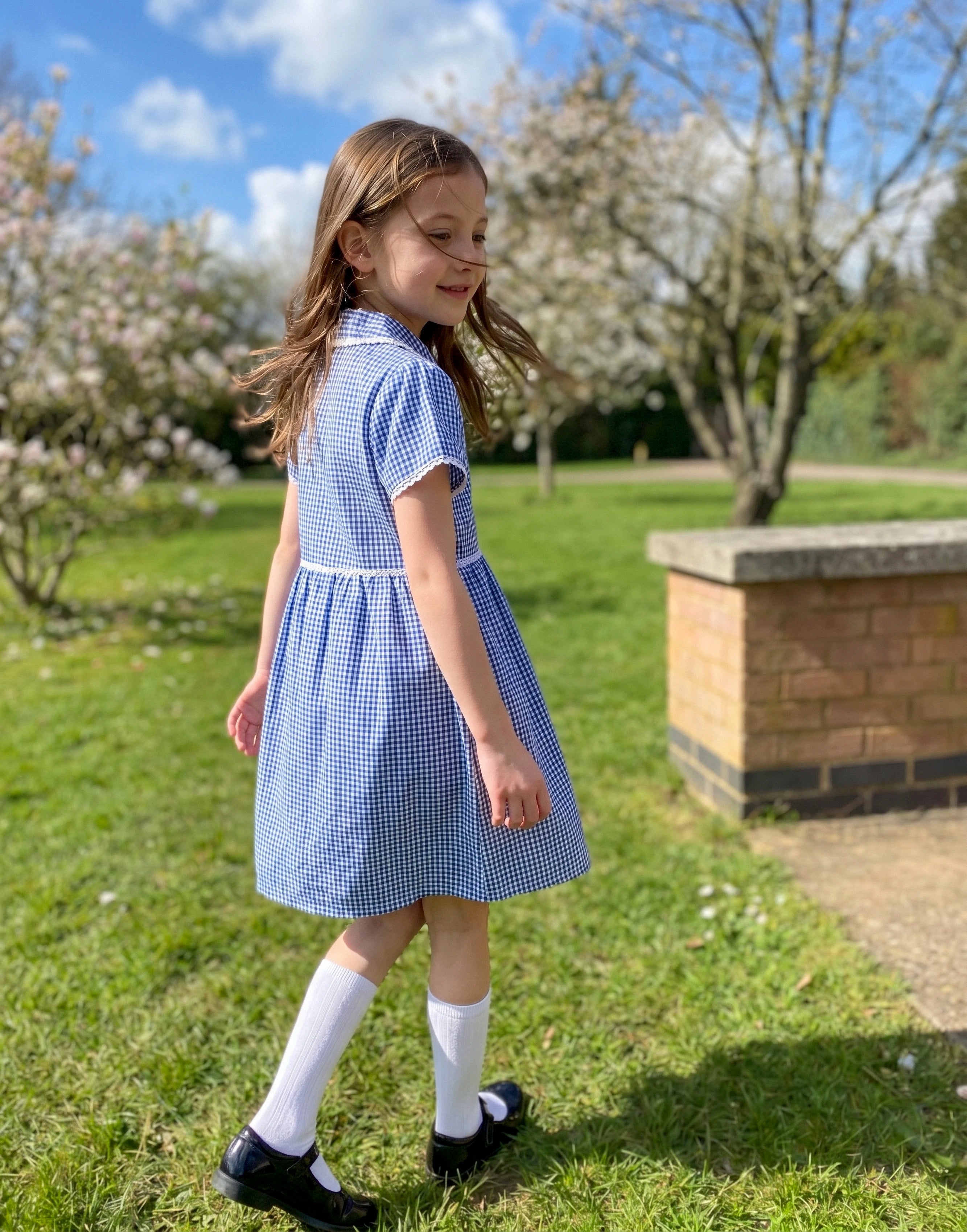 Girl wearing a blue gingham summer school dress made from 100% GOTS-certified organic cotton, back view.