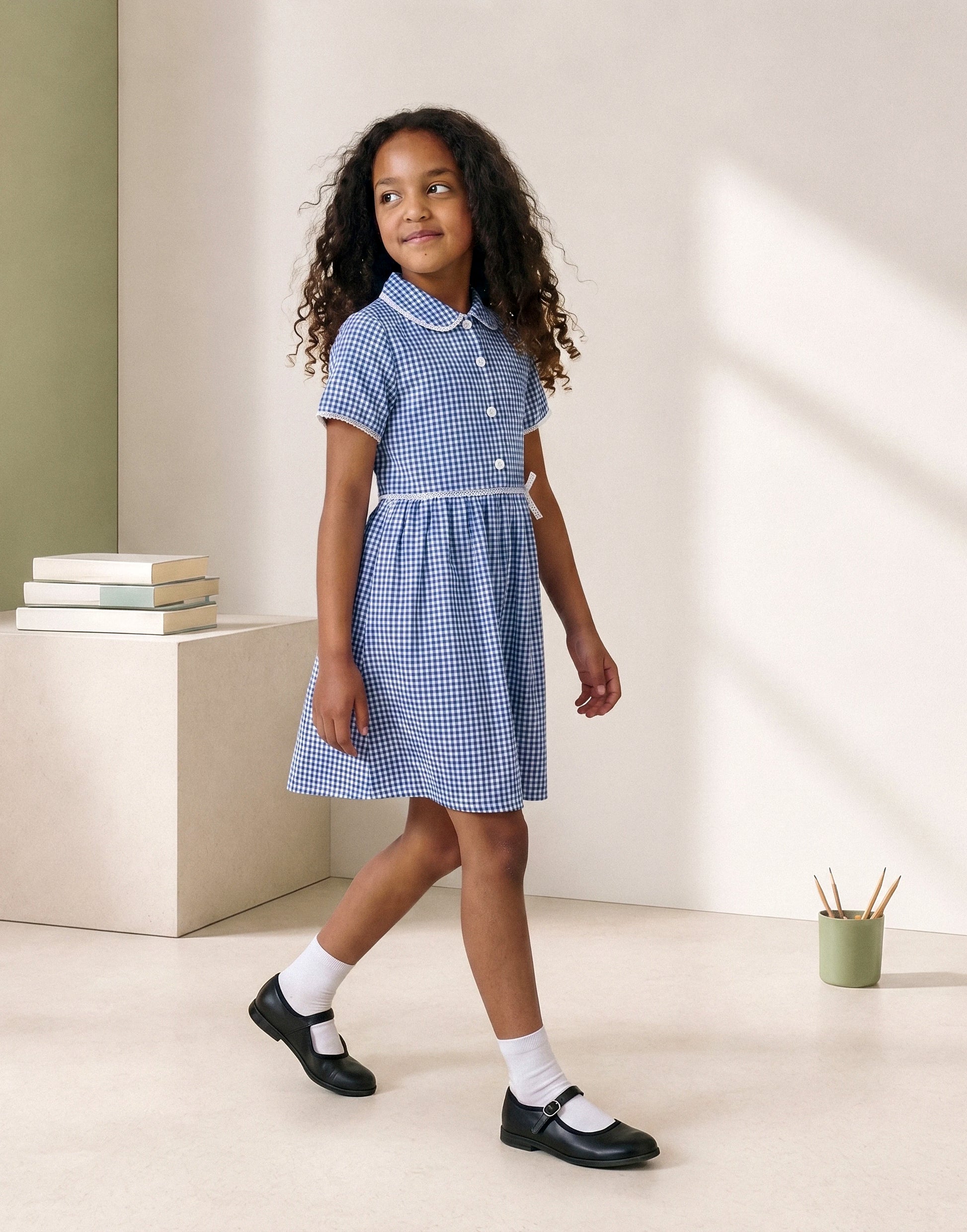 Girl wearing a blue gingham summer school dress made from 100% GOTS-certified organic cotton, front view.