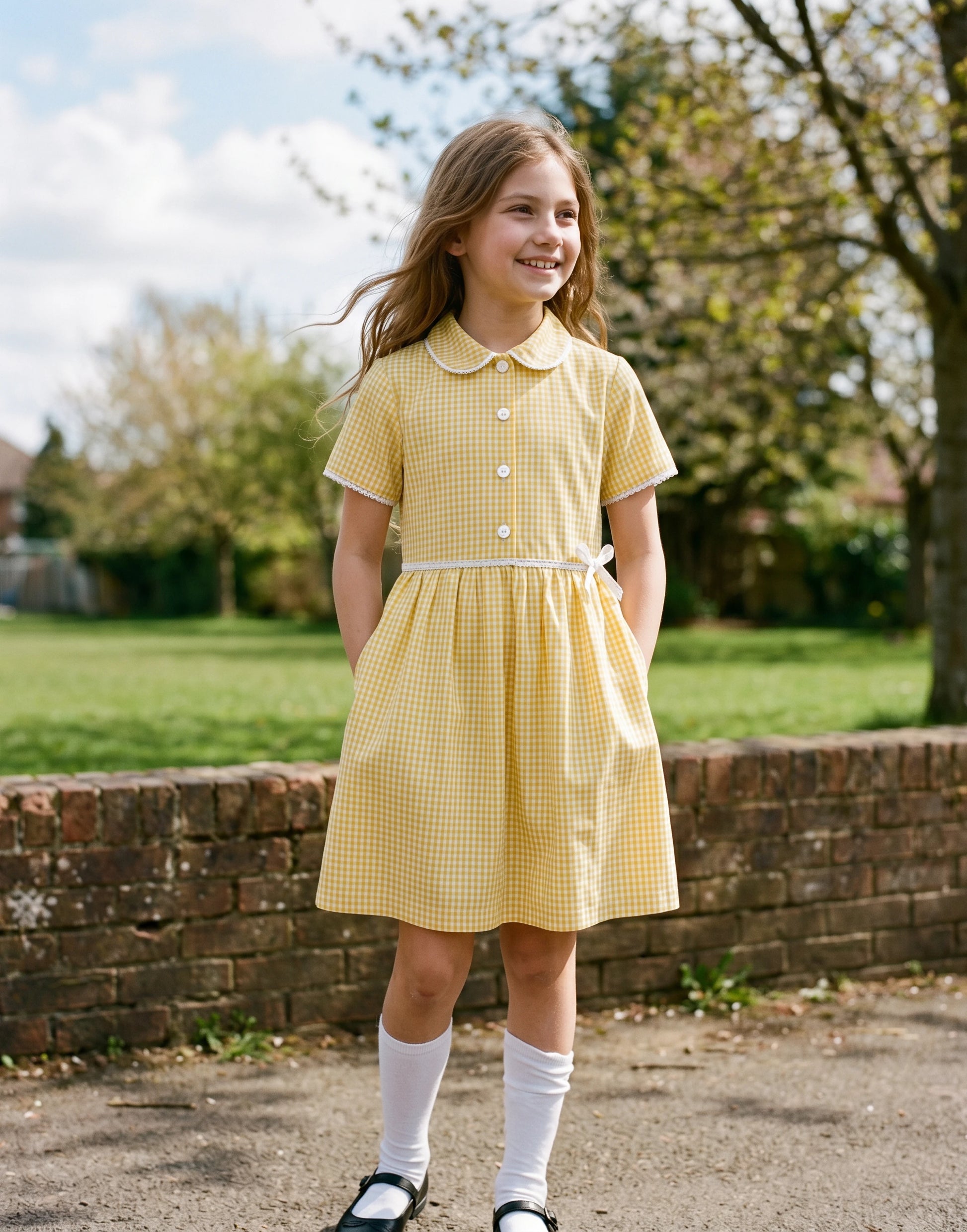 Girl wearing a yellow gingham summer school dress made from 100% GOTS-certified organic cotton, front view.