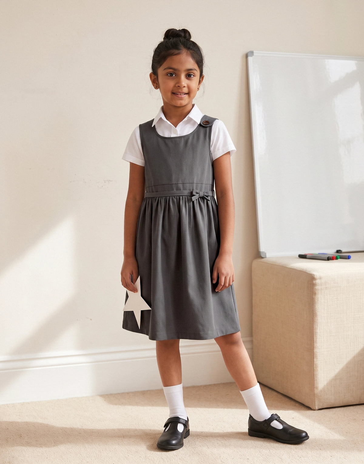 Girl wearing a grey school pinafore dress with bow made from 100% GOTS-certified organic cotton.