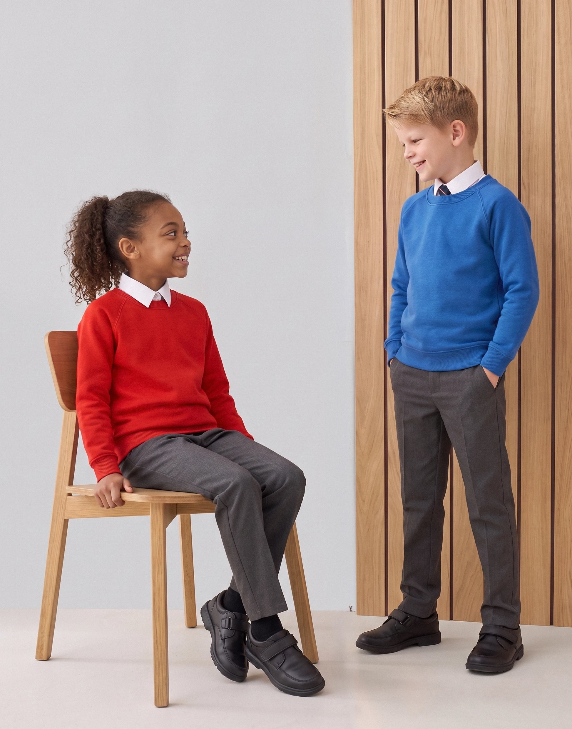Children wearing a royal blue and red organic cotton school sweatshirt with a classic crew neck, front view.