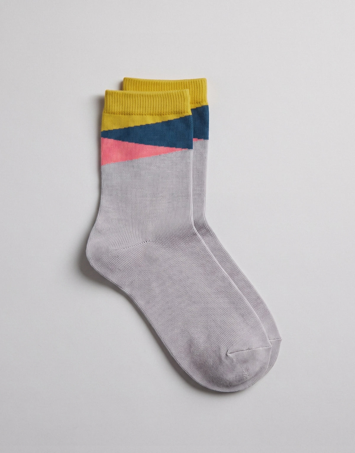 A pair of light gray crew socks with geometric color-blocked stripes in yellow, navy blue, and pink near the cuff, displayed on a light gray background.
