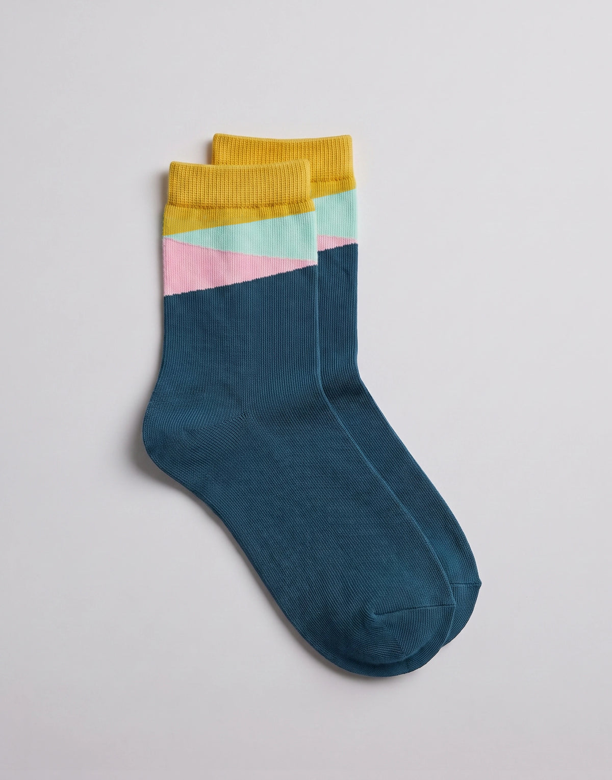 A pair of crew socks in a dark teal blue, featuring a color-blocked cuff with yellow, light pink, and mint green stripes, displayed on a light gray background.