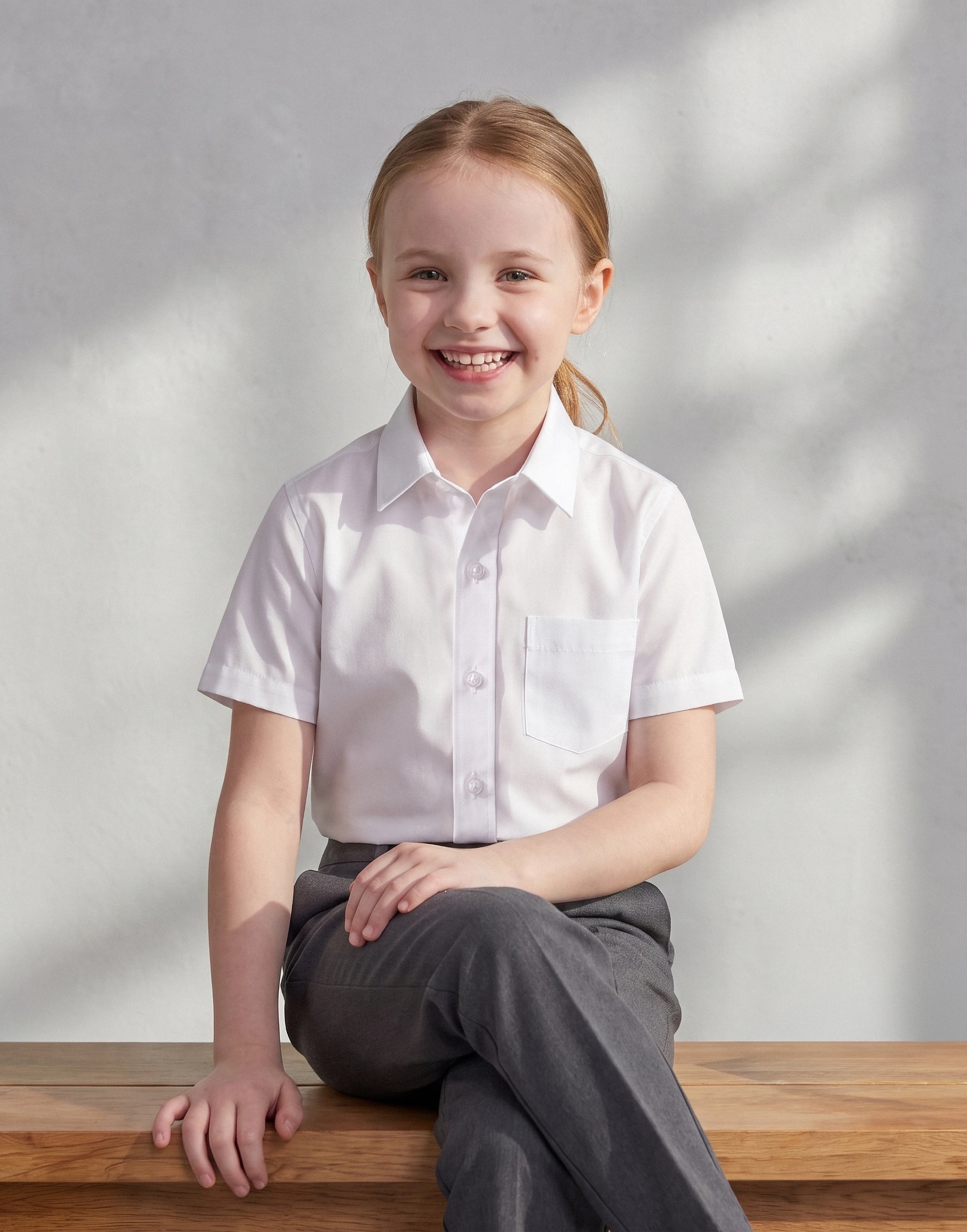 Child wearing a white short sleeve school shirt made from 100% organic cotton, front view.