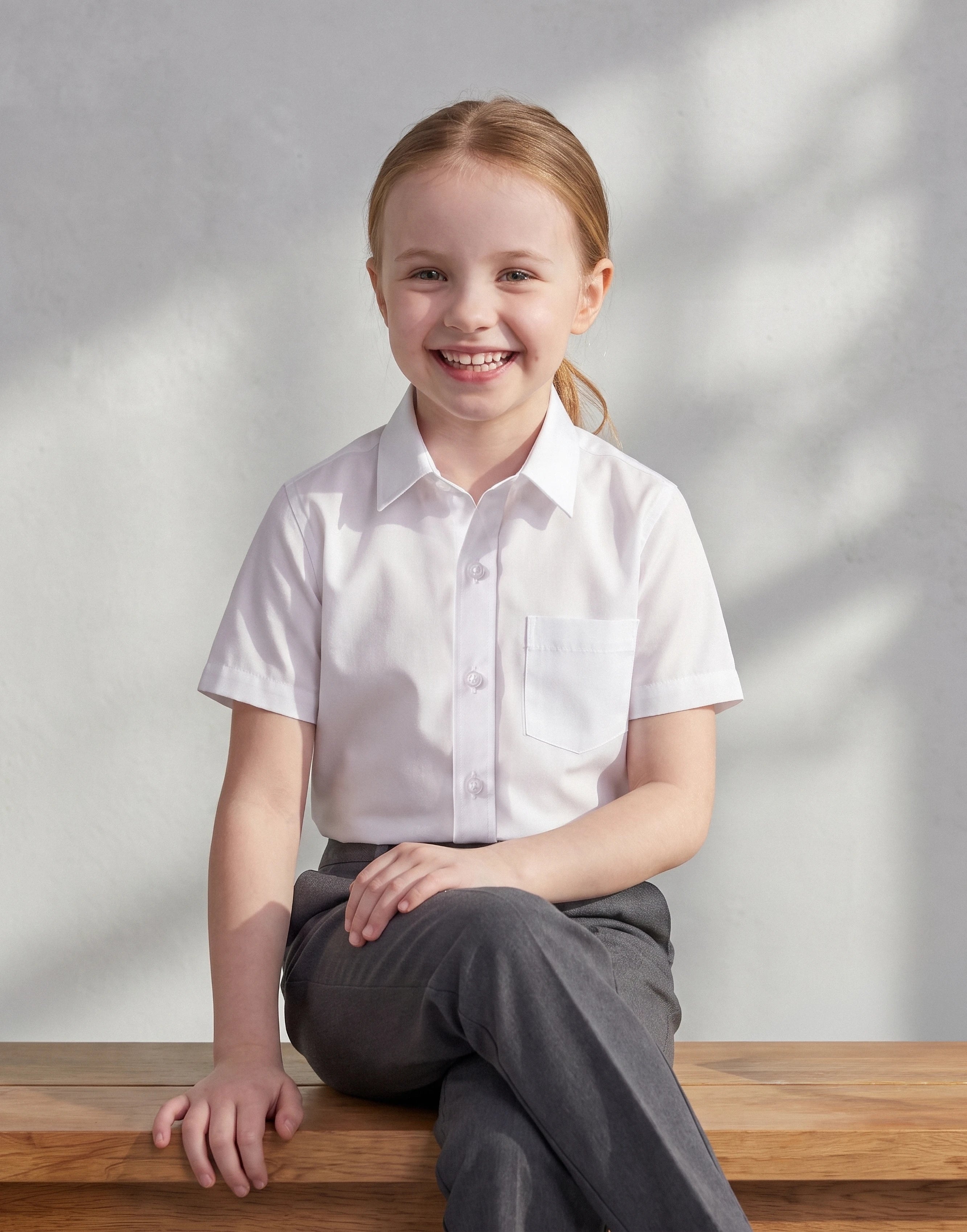 Child wearing a white short sleeve school shirt made from 100% organic cotton, front view.
