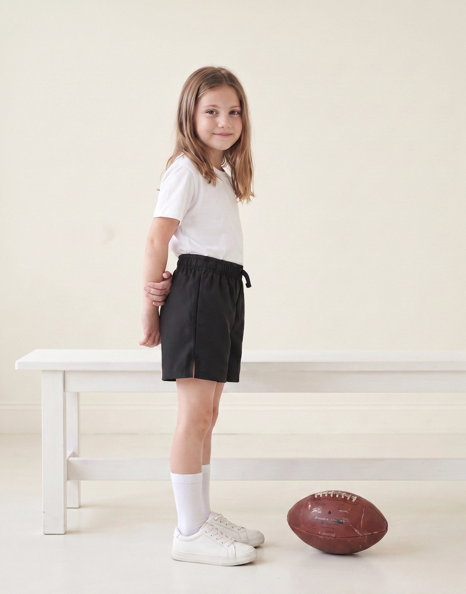 Child wearing black organic cotton unisex PE shorts, side view.