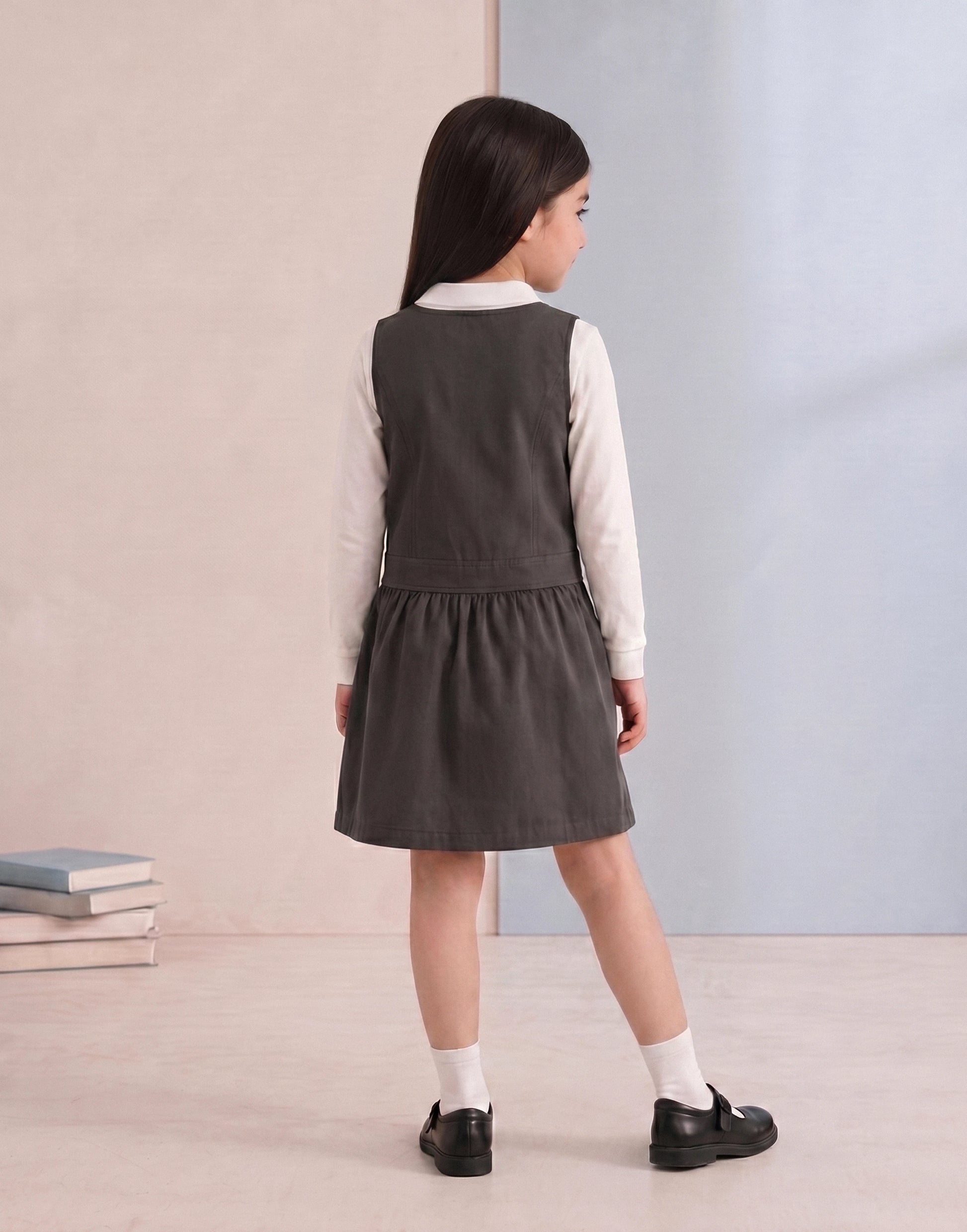Girl wearing a grey organic cotton school pinafore, back view.